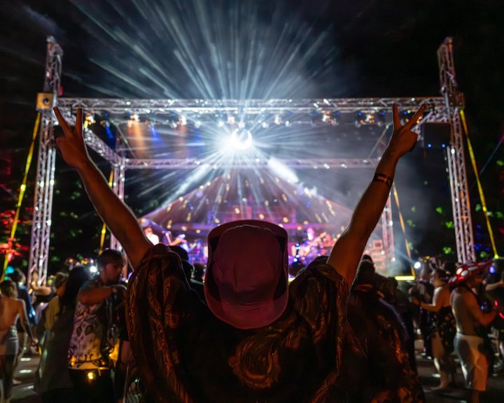 Festival attendee raising both arms beneath bright stage lights